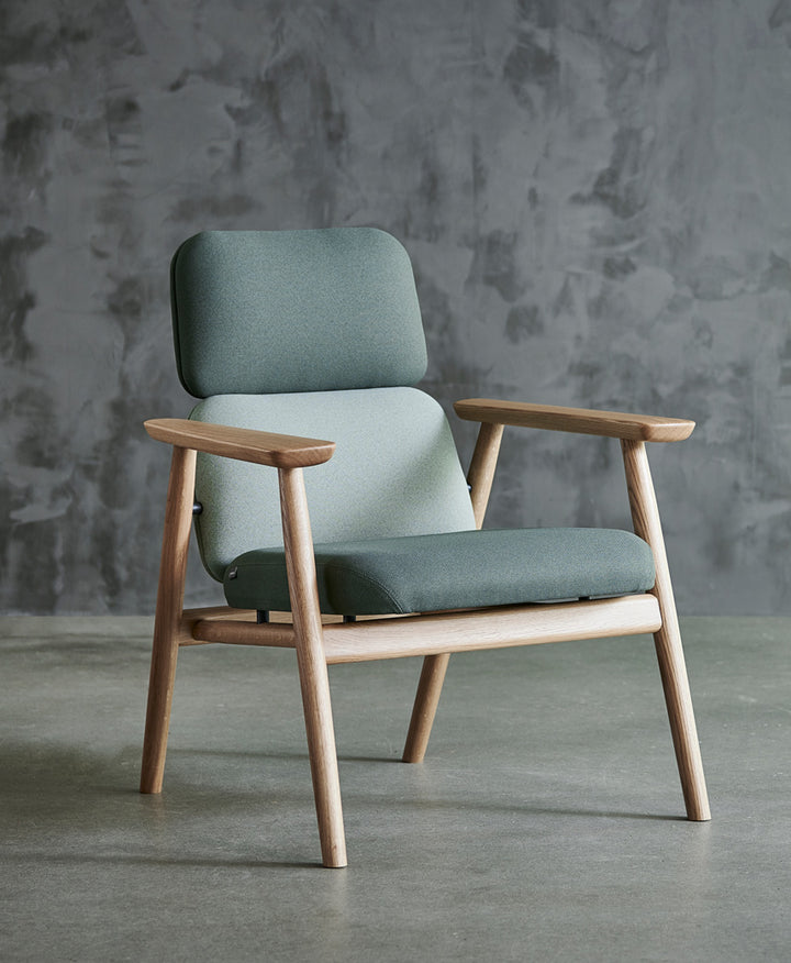 Lænestol / Loungestol, model Bear L, stel i massiv natur eg og polster i to nuancer grøn tekstil, den står på beton gulv foran rustik væk