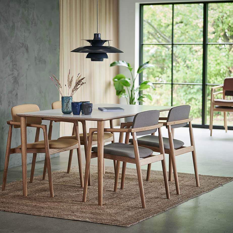 Spisetue med beton og lamelvæg og stort vinduesparti i baggrunden, spisebord med egetræs ben og hvid bordplade, model Care Table 3900, med 4 af den stabelbare spisebordsstol Nobel 8905 stående rundt om